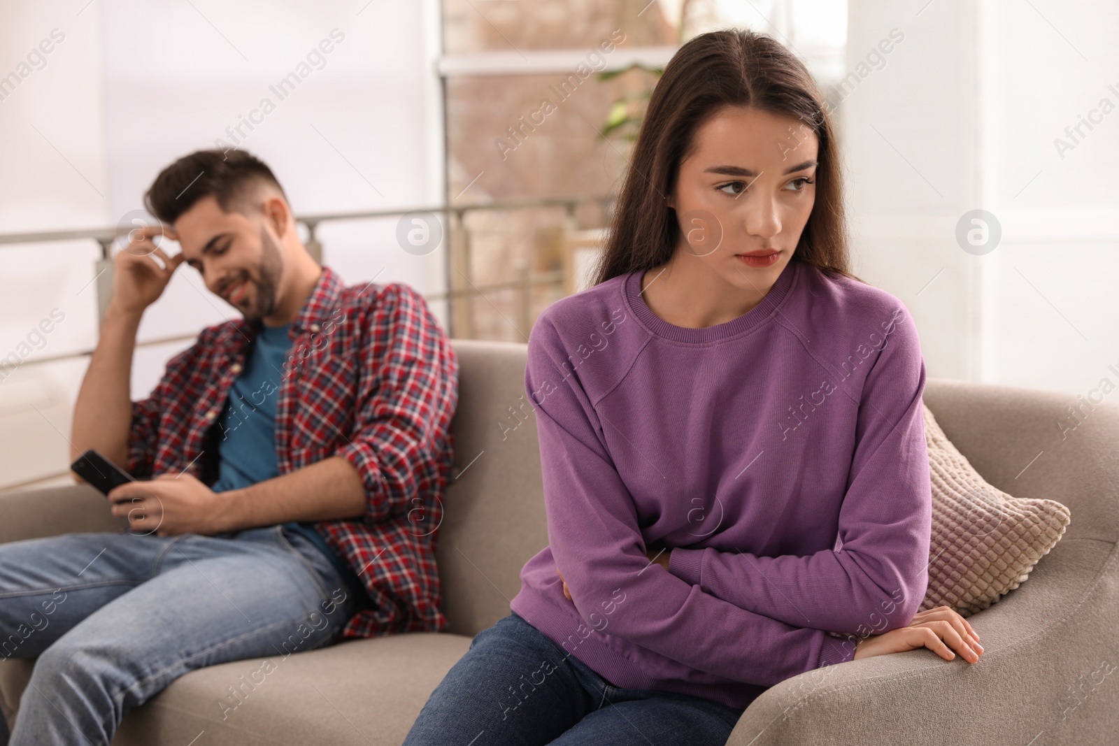 Photo of Young man preferring smartphone over his girlfriend on couch at home