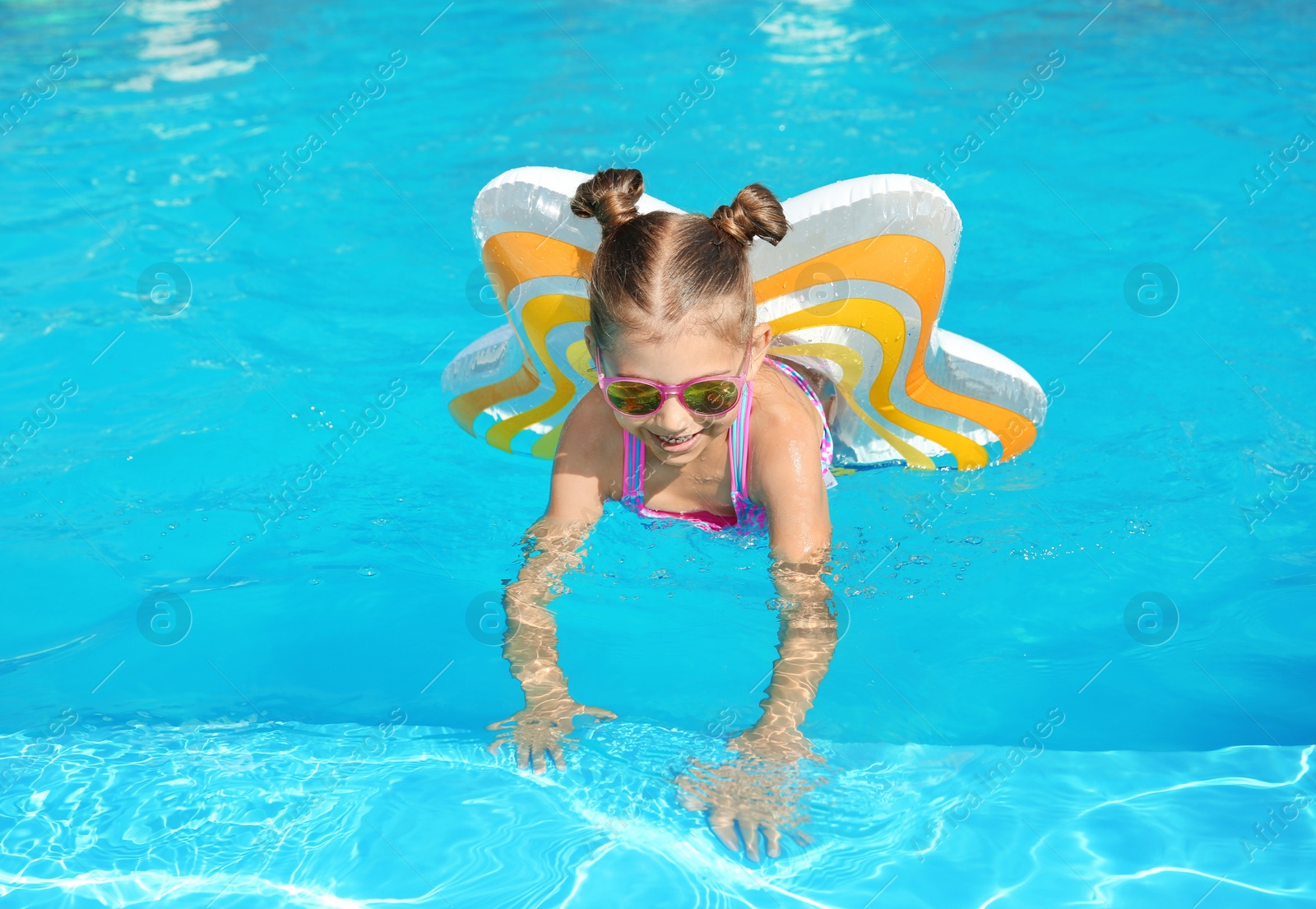 Photo of Little girl with inflatable ring in swimming pool on sunny day