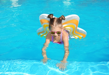 Little girl with inflatable ring in swimming pool on sunny day