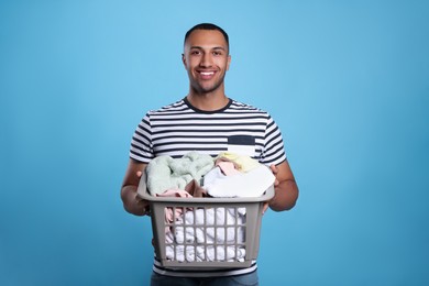 Photo of Happy man with basket full of laundry on light blue background