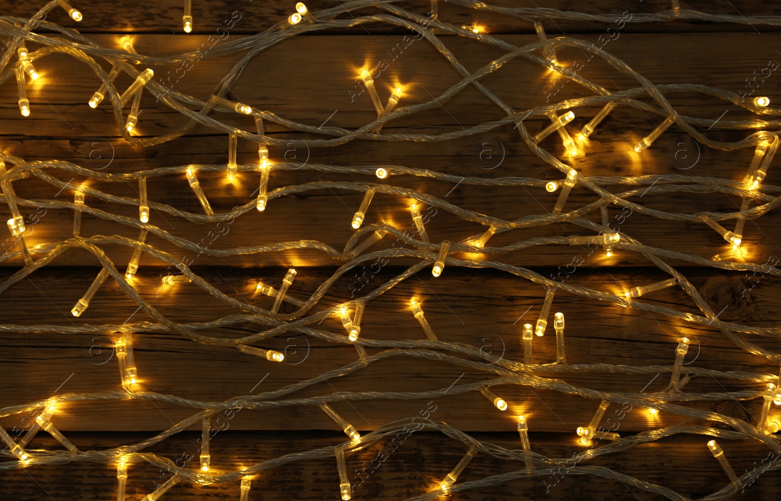 Photo of Glowing Christmas lights on wooden background, top view