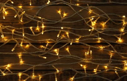 Photo of Glowing Christmas lights on wooden background, top view