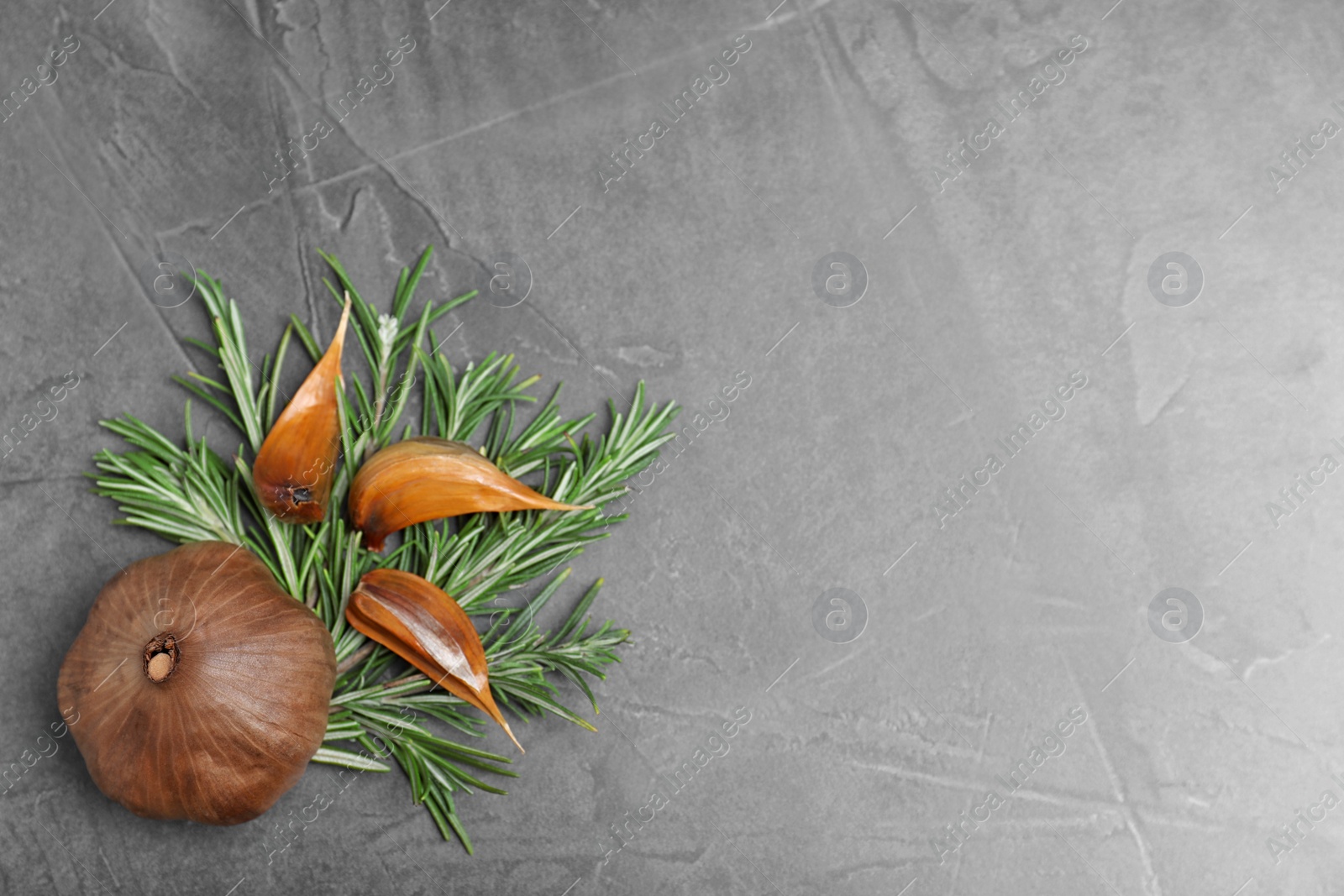 Photo of Flat lay composition with aged black garlic and rosemary on gray background. Space for text