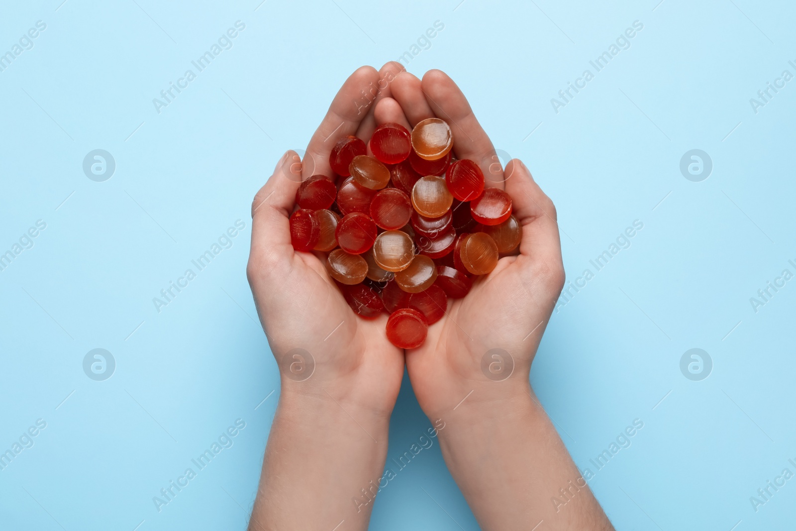 Photo of Woman holding handful of cough drops on light blue background, top view