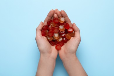 Woman holding handful of cough drops on light blue background, top view