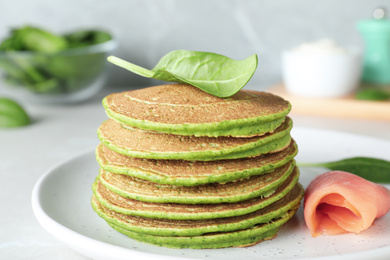 Tasty spinach pancakes with salmon on light grey table, closeup