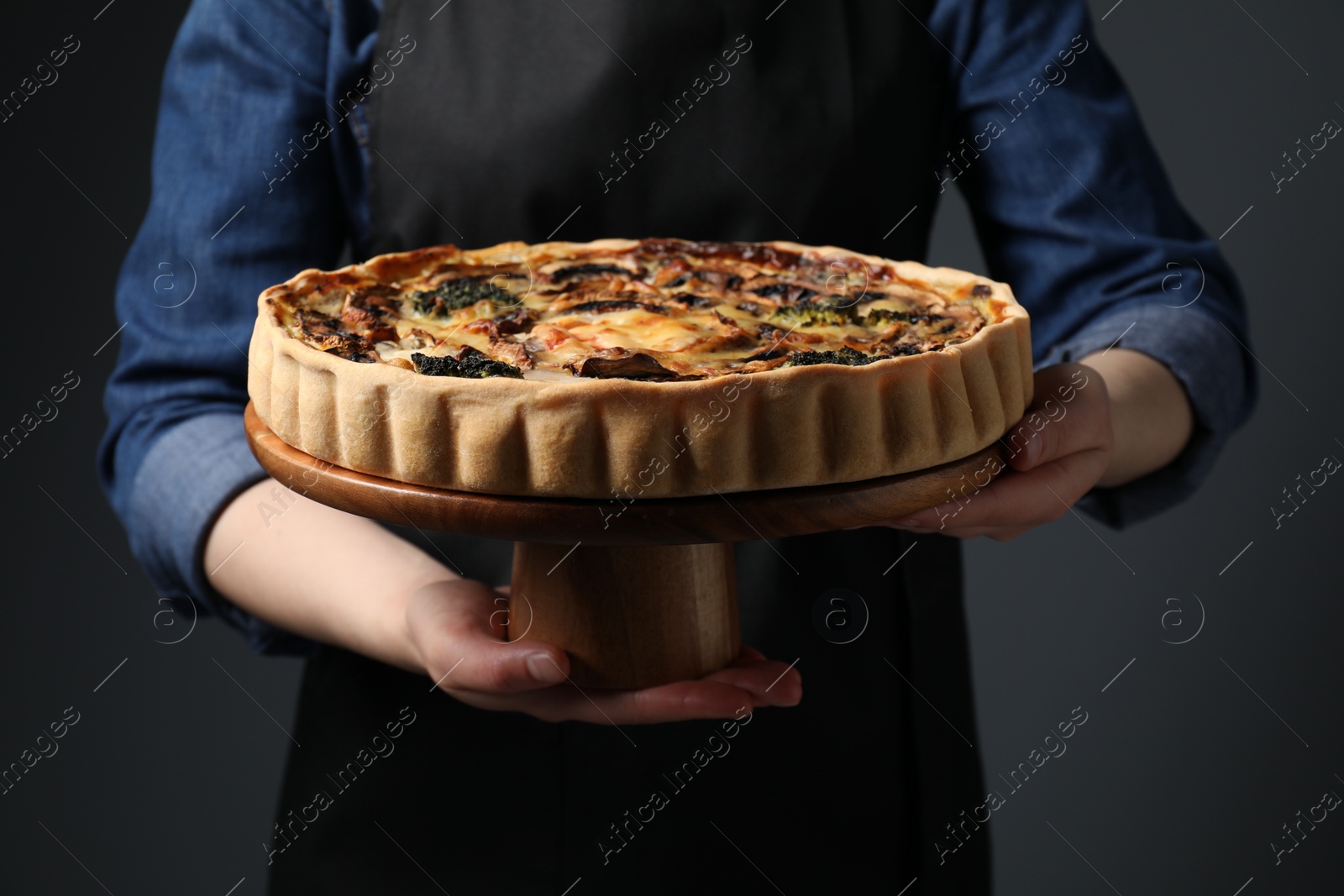 Photo of Woman holding delicious quiche with mushrooms on dark grey background, closeup