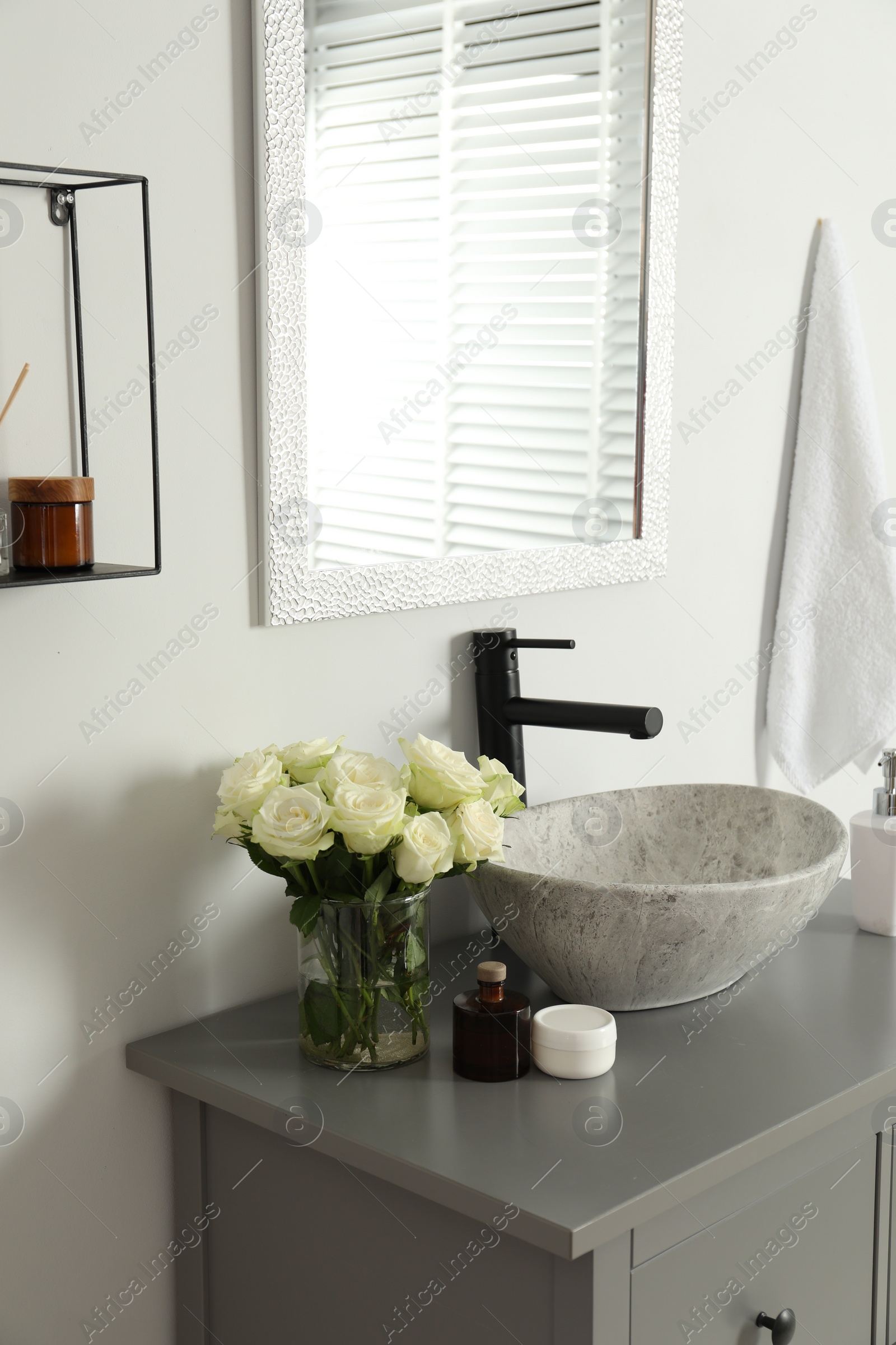 Photo of Vase with beautiful white roses and toiletries near sink in bathroom