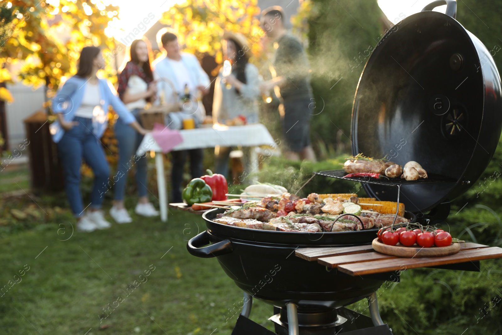 Photo of Group of friends having party outdoors. Focus on barbecue grill with food. Space for text