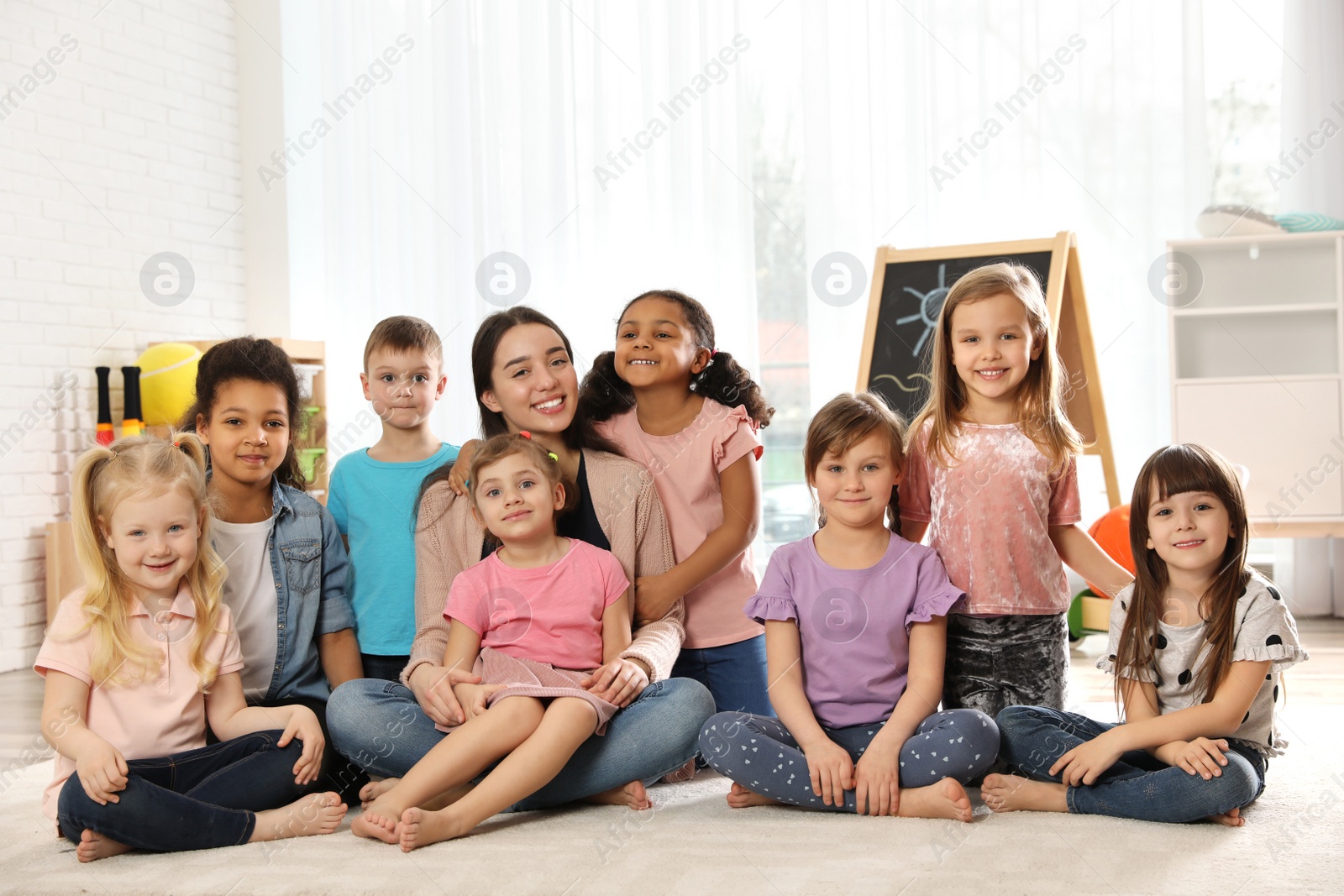 Photo of Group of cute little children with teacher sitting on floor in kindergarten