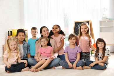 Photo of Group of cute little children with teacher sitting on floor in kindergarten