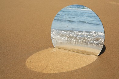 Photo of Round mirror reflecting sea on sandy beach