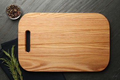 Photo of Wooden cutting board and spices on dark grey table, flat lay