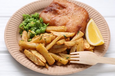 Tasty fish, chips, peas and lemon on white wooden table, closeup