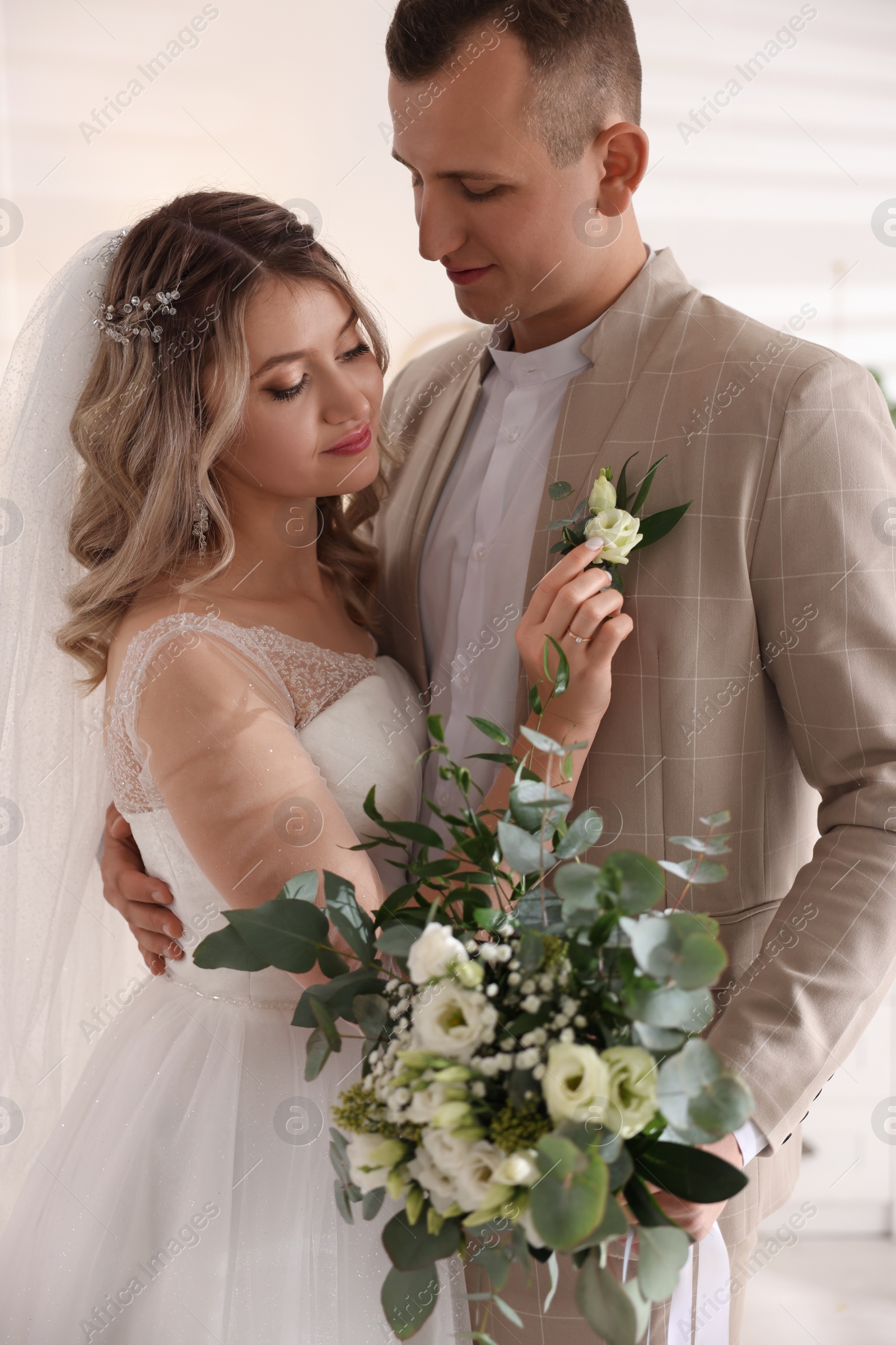 Photo of Happy groom with bouquet and bride indoors. Wedding day