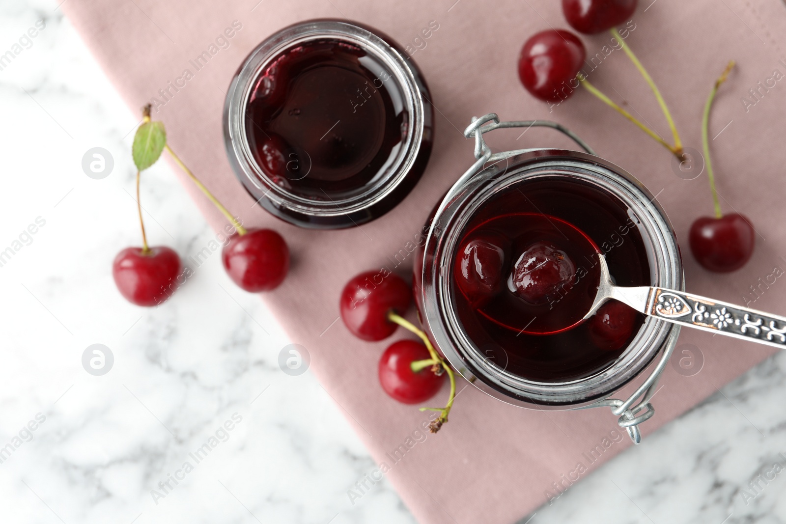 Photo of Jars of pickled cherries and fresh fruits on white marble table, top view