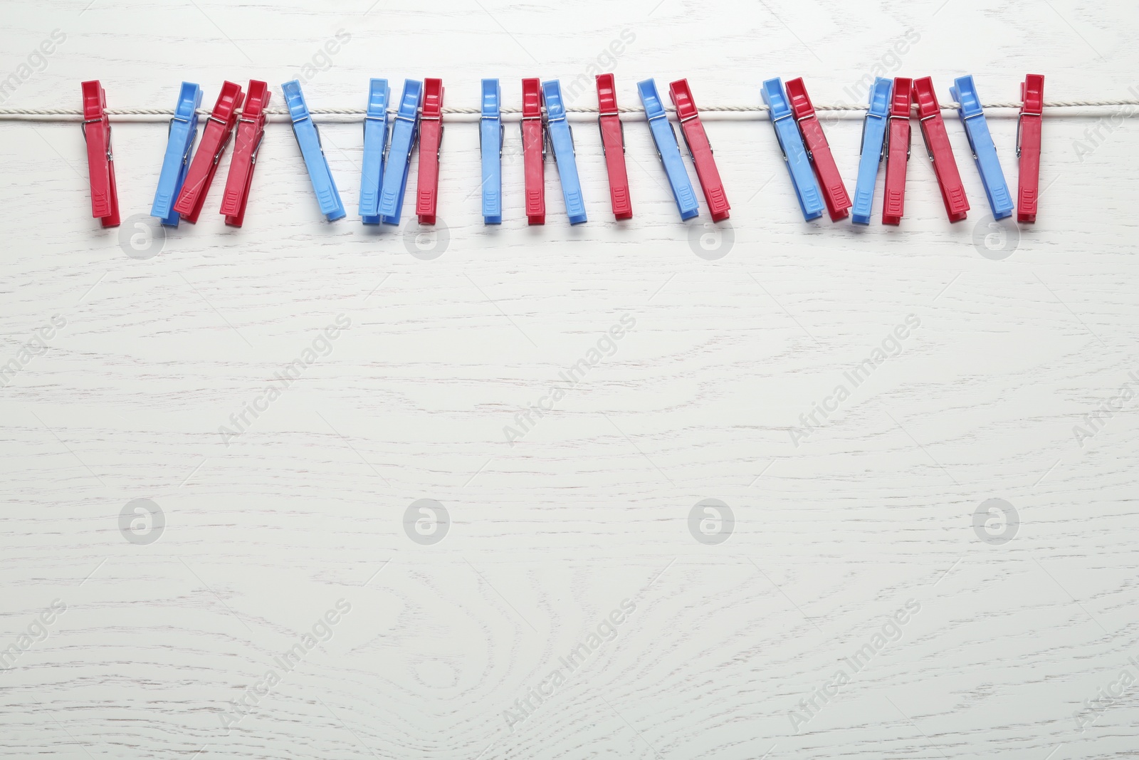 Photo of Colorful plastic clothespins and rope on white wooden background. Space for text