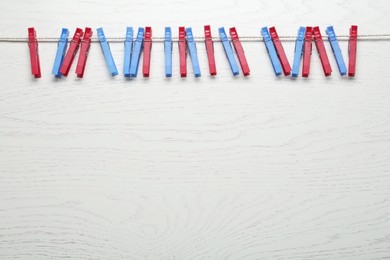 Colorful plastic clothespins and rope on white wooden background. Space for text