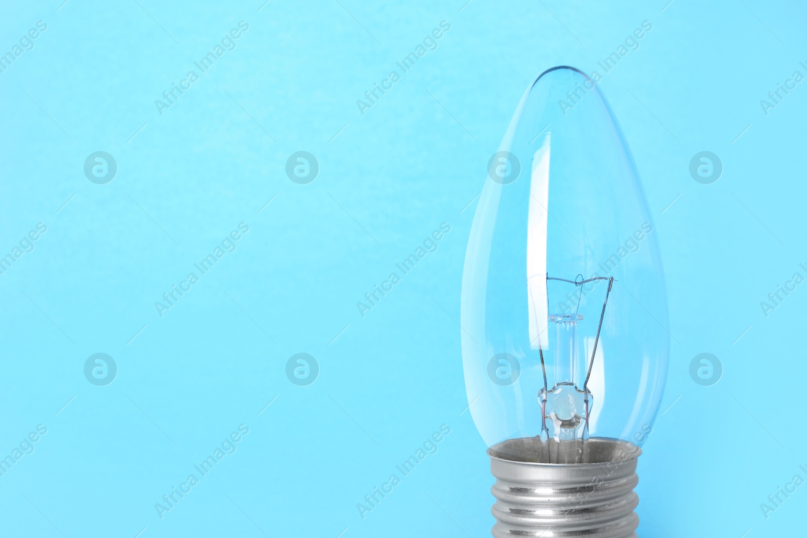 Photo of New modern lamp bulb on light blue background, space for text