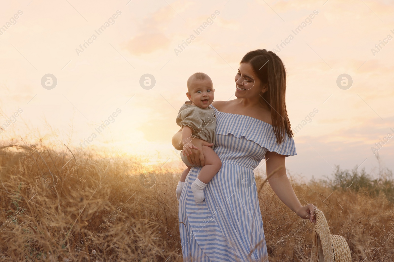 Photo of Happy mother with adorable baby in field at sunset, space for text