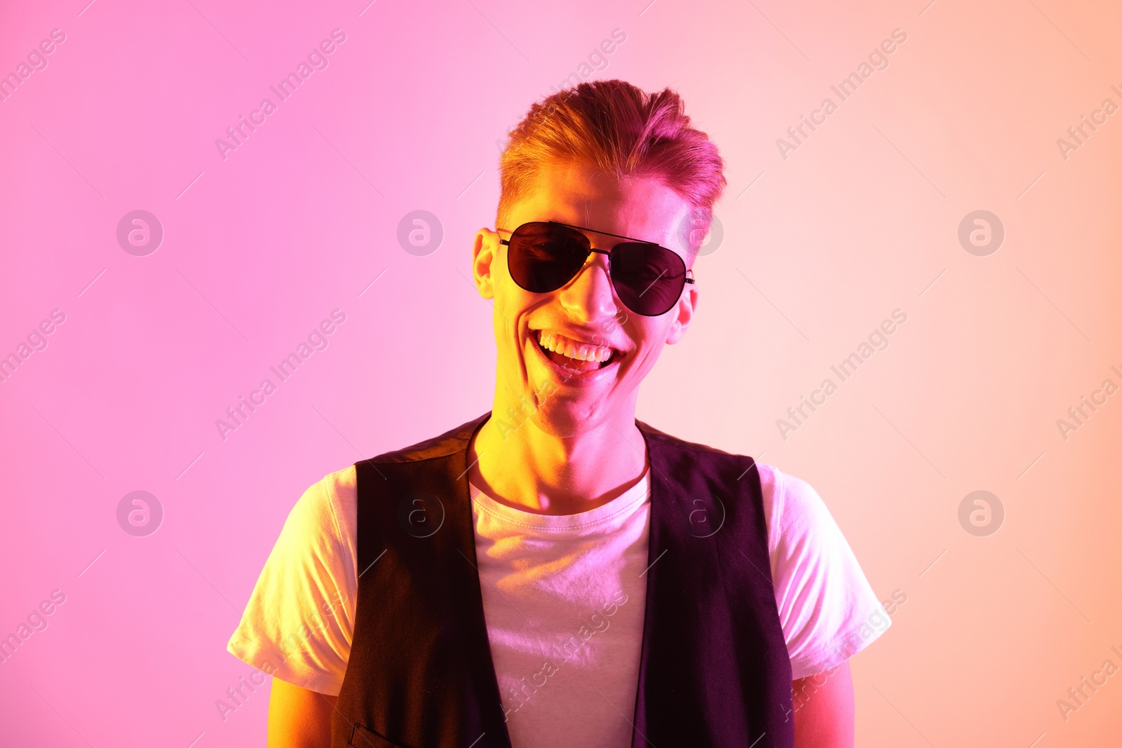 Photo of Stylish young man in sunglasses on pink background in neon lights