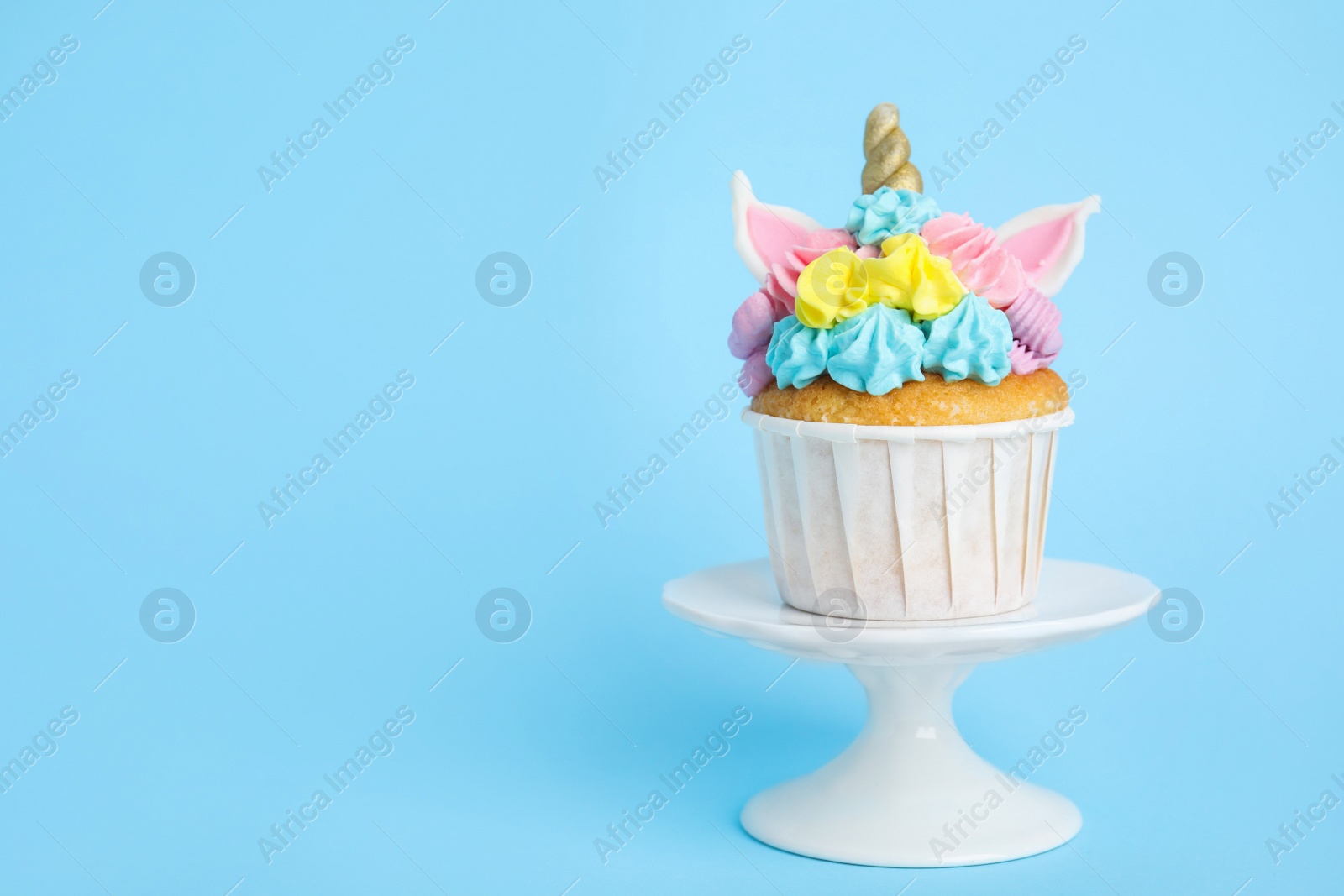 Photo of Dessert stand with cute sweet unicorn cupcake on light blue background. Space for text