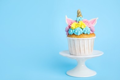 Dessert stand with cute sweet unicorn cupcake on light blue background. Space for text