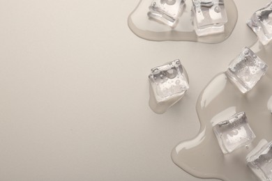 Photo of Melting ice cubes and water drops on light grey background, flat lay. Space for text