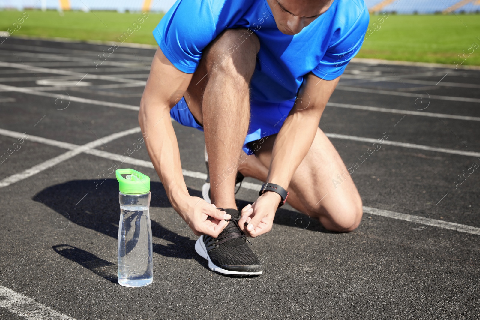 Photo of Sporty man tying shoelaces near bottle of water at stadium on sunny day