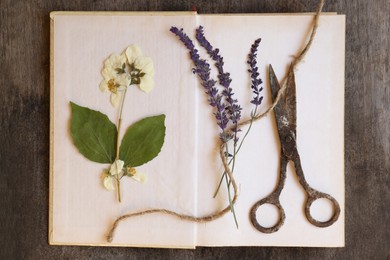 Photo of Open book with beautiful dried flowers, old scissors and twine on wooden table, top view