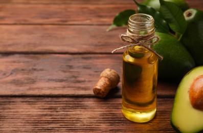 Photo of Glass bottle of cooking oil and fresh avocados on wooden table, closeup. Space for text