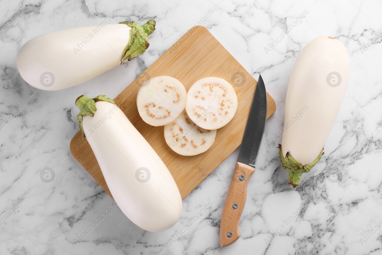 Photo of Wooden board, raw white eggplants and knife on marble table, flat lay