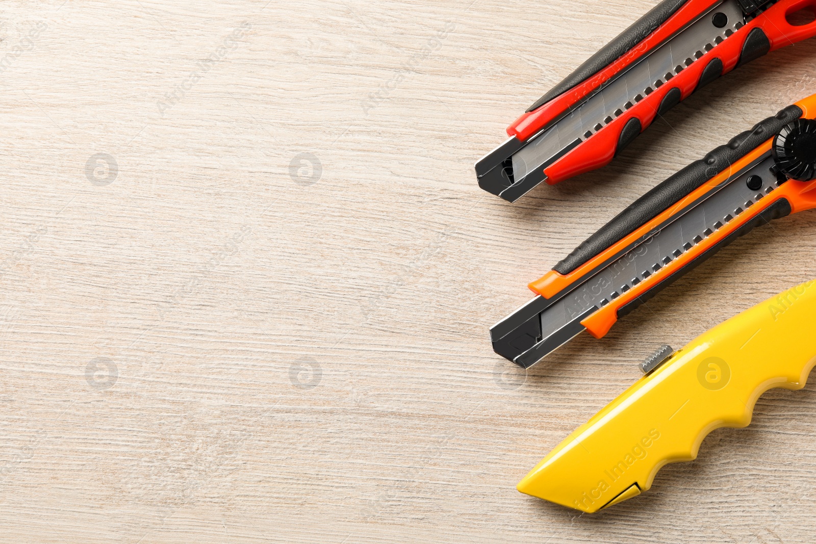 Photo of Different utility knives on white wooden table, flat lay. Space for text