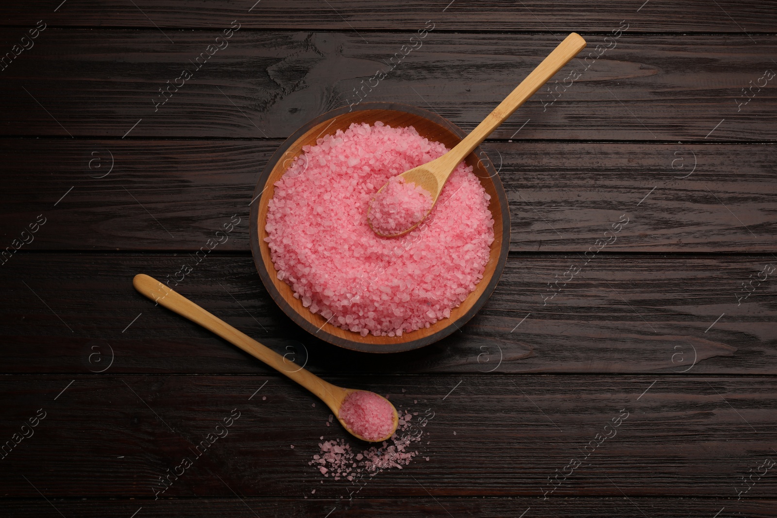 Photo of Bowl and spoons with pink sea salt on wooden table, flat lay