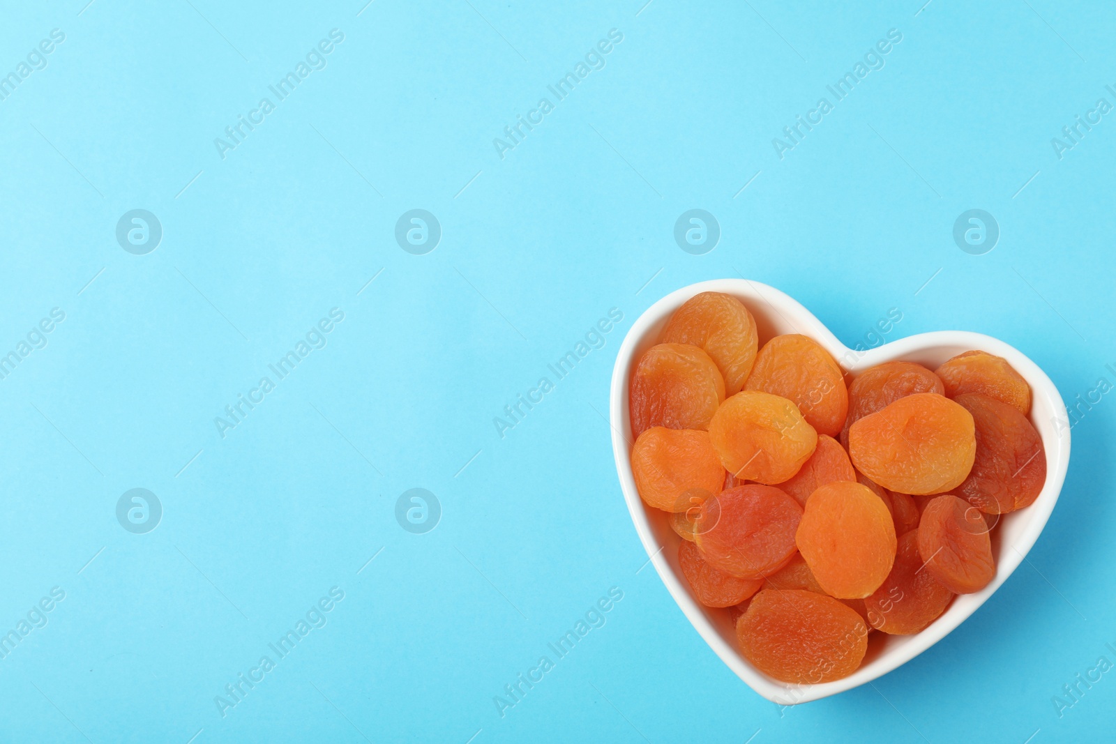 Photo of Bowl of dried apricots on color background, top view with space for text. Healthy fruit