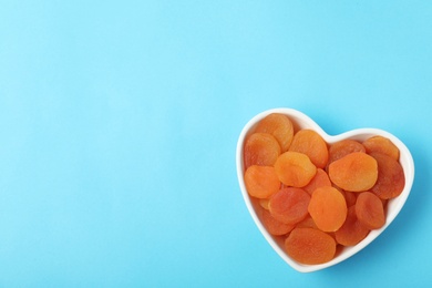 Photo of Bowl of dried apricots on color background, top view with space for text. Healthy fruit