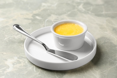 Photo of Plate with knife and bowl of clarified butter on grey background