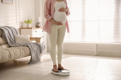 Pregnant woman standing on scales at home, closeup