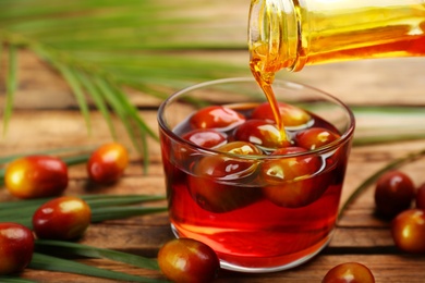 Pouring fresh palm oil into glass on wooden table, closeup