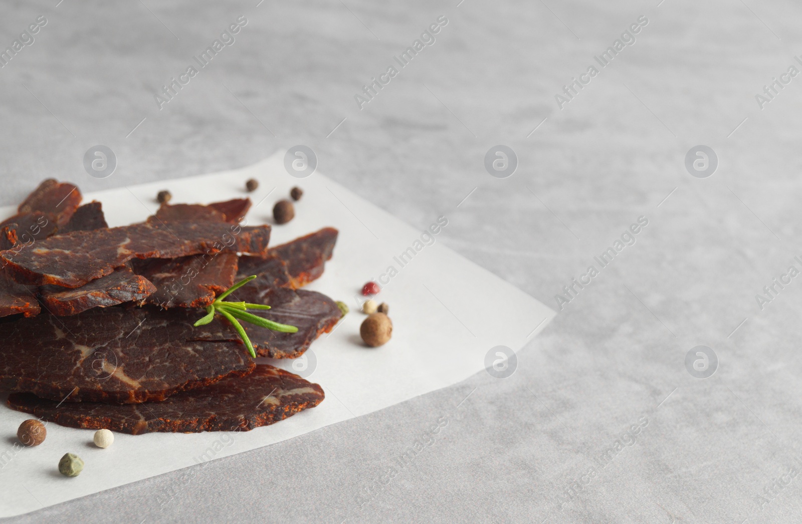 Photo of Pieces of delicious beef jerky and spices on light grey table. Space for text