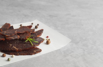 Photo of Pieces of delicious beef jerky and spices on light grey table. Space for text