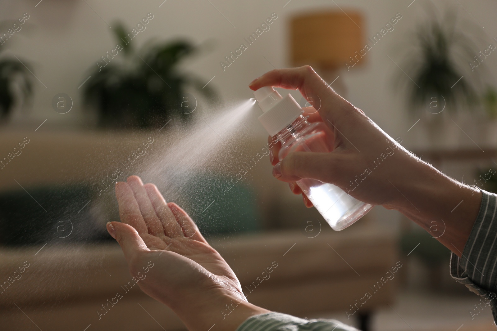 Photo of Woman spraying antiseptic onto hand indoors, closeup