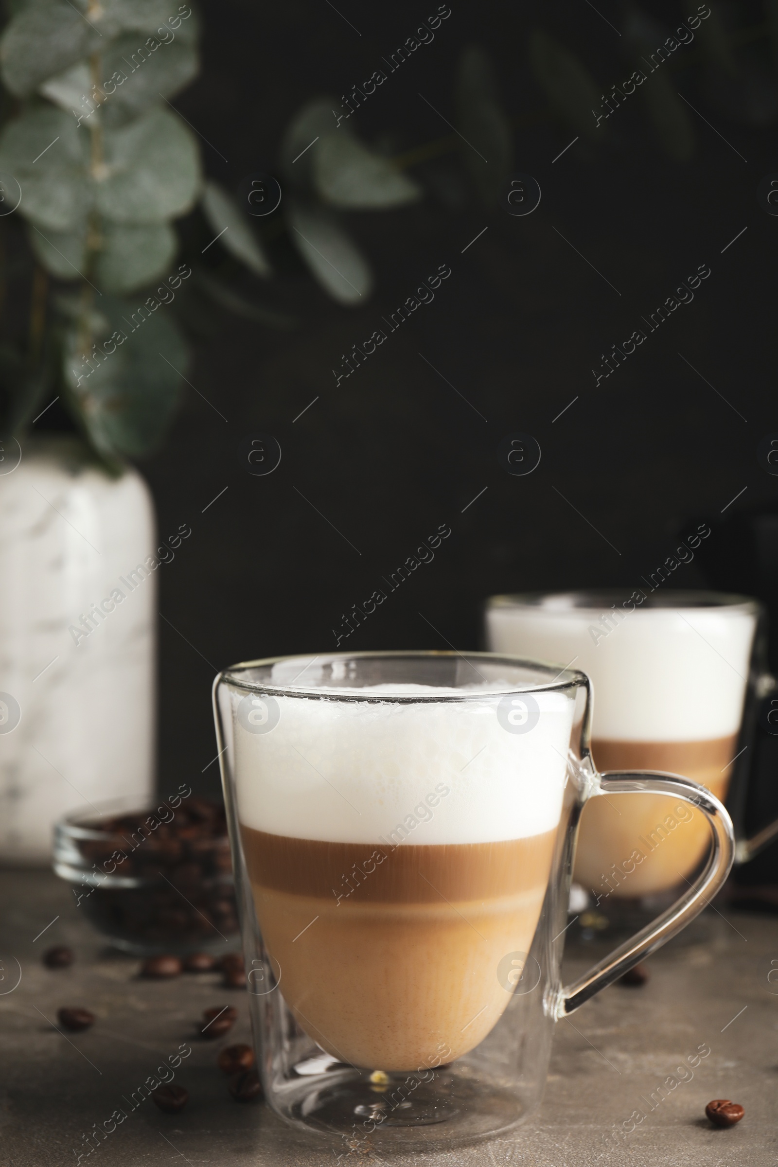 Photo of Glass cups of delicious latte macchiato and scattered coffee beans on grey table