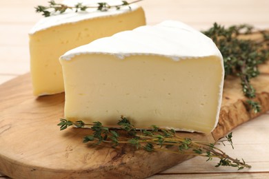 Photo of Board with pieces of tasty camembert cheese and thyme on light wooden table, closeup