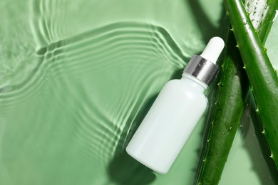 Bottle of cosmetic product and aloe leaves in water on pale green background, flat lay. Space for text