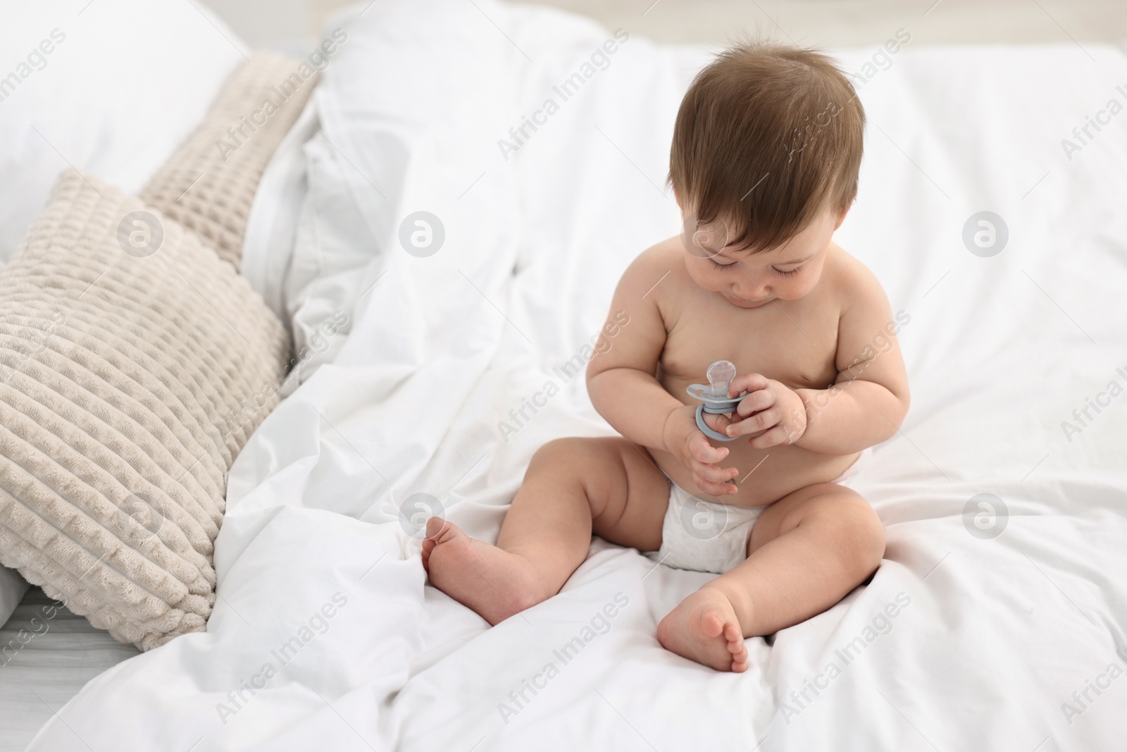 Photo of Cute baby boy with pacifier on bed at home