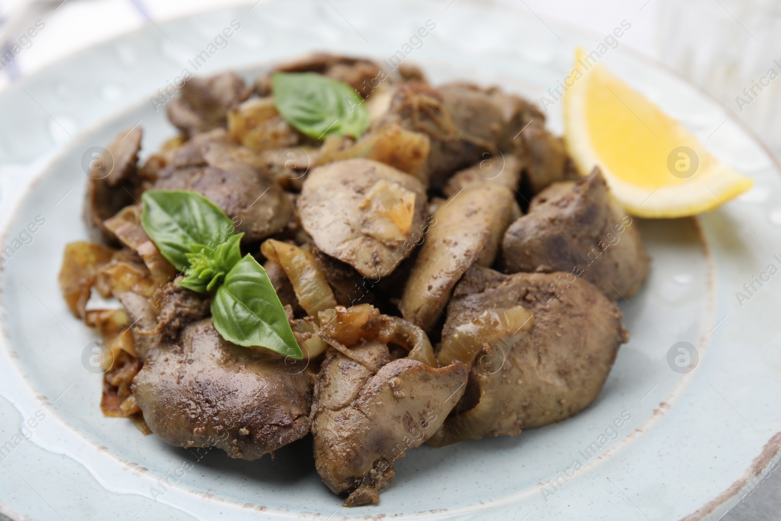 Photo of Delicious fried chicken liver with onion and basil on table, closeup