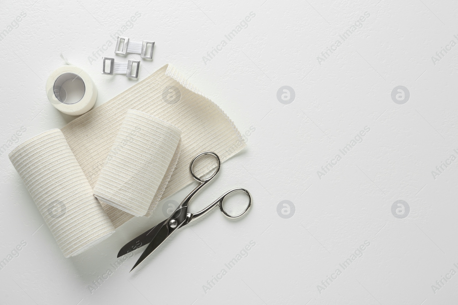 Photo of Medical bandage rolls, sticking plaster and scissors on white table, flat lay. Space for text