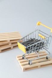 Metal nails in shopping cart on light grey background