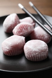 Photo of Delicious mochi and chopsticks on black plate, closeup. Traditional Japanese dessert